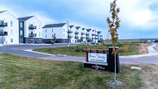 A sign for a development called "Pine Ridge Townhomes" is in front of a grassy area with apartment buildings in the background.
