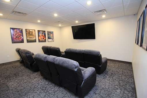 A black leather couch in a room with a television and pictures on the wall.