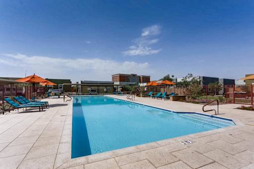 A large outdoor swimming pool surrounded by a patio and lounge chairs.