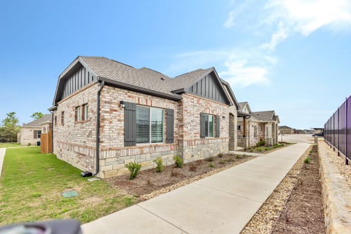 an exterior view of a brick house with a sidewalk and grass at Avilla Towne Center Apartments, Texas, 75407