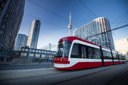 A red and white train is on a track in a city with tall buildings.