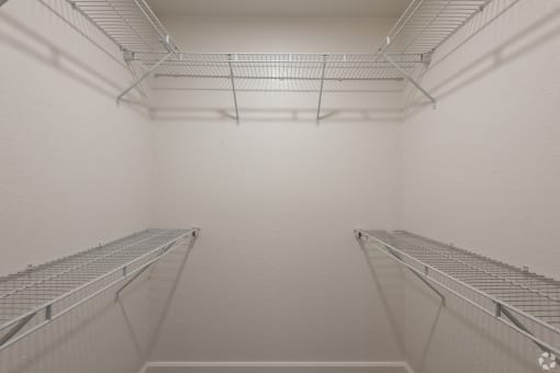 the walk in closet in a white room with two empty shelves