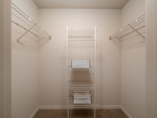 a walk in closet in a small room with white walls and white shelves and racks at The Fountains Apartments, Pensacola, Florida