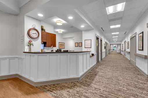 A hallway with a clock on the wall and pictures on the walls.