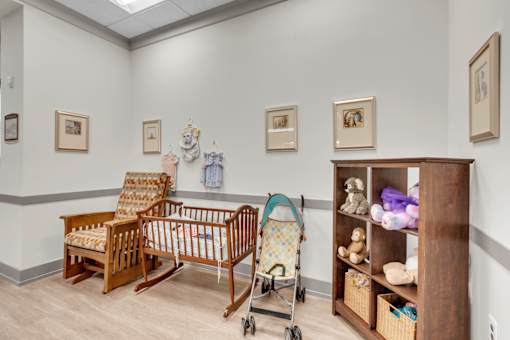 A baby nursery with a rocking chair, crib, and shelf with toys.