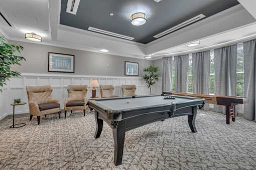 A room with a pool table and chairs.