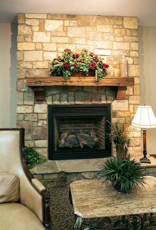 A stone fireplace with a wooden mantle and a plant on top.