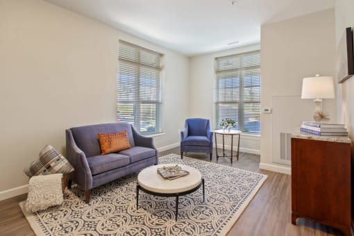 A living room with a grey couch, a coffee table, and a blue chair at White Springs Senior Living, Warrenton, 20186