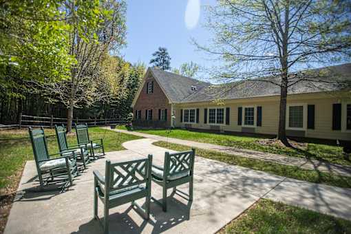 A sunny day at a park with a bench and a building in the background.at Spring Arbor of Williamsburg, Virginia