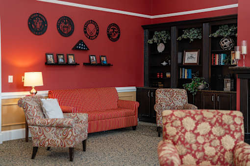 A living room with a red couch, two chairs, and a bookcase at Spring Arbor of Cary in Cary, NC