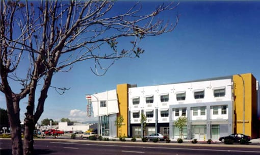 A modern building with a yellow and white facade is surrounded by trees and cars.