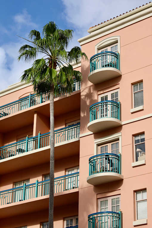 A tall pink building with balconies and a palm tree in front.
