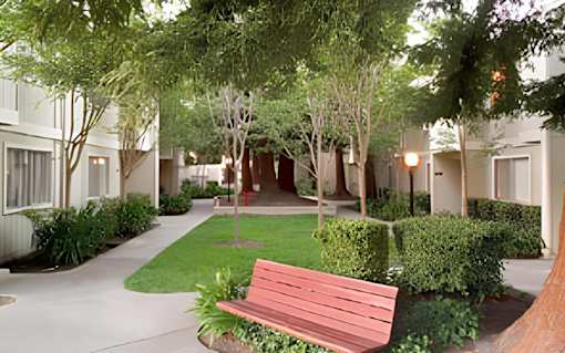 A red bench sits in the middle of a grassy area between two buildings.
