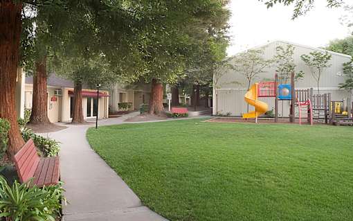 A playground with a yellow slide and a red bench.