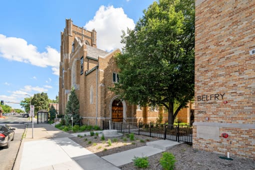 the outside of a brick church with a sidewalk and a tree