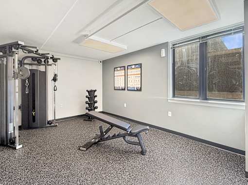 A gym room with a bench, weights, and a window.