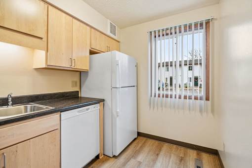 A kitchen with a white refrigerator, wooden cabinets, and a window with blinds.