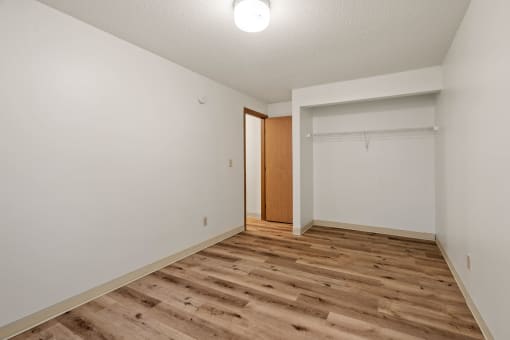 a spacious living room with white walls and wood flooring and a closet