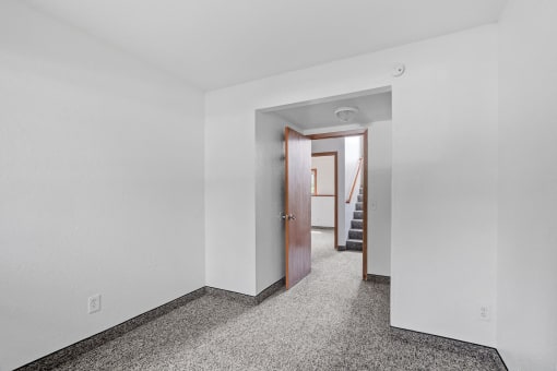 a bedroom with white walls and a door to a hallway with stairs