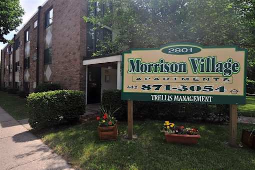 A sign for Morrison Village Apartments is in front of a brick building.