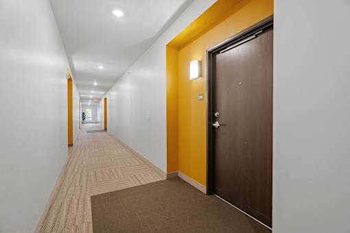 a hallway with white walls and a wooden floor and a brown door