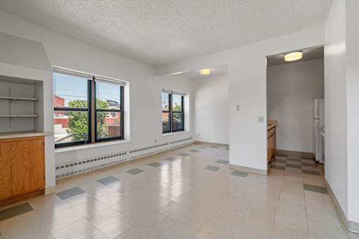 an empty living room and kitchen with large windows and tiled floors