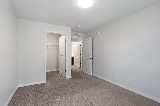 a bedroom with white walls and carpet and a door to a closet