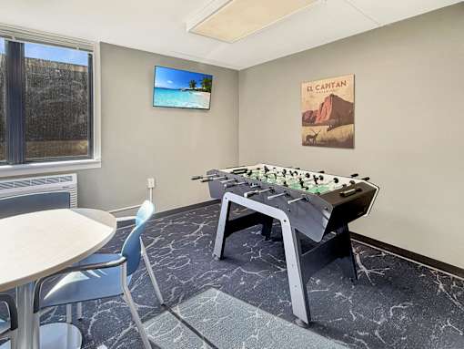 A foosball table is in the middle of a room with a TV and a picture on the wall.