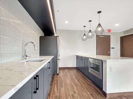 A modern kitchen in the Skydeck Lounge with dark wood floors and white countertops.