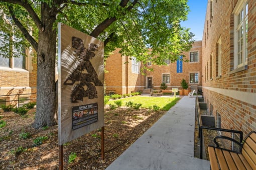 a sign in front of a brick building with a tree and benches
