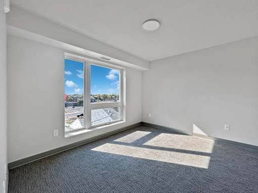 a living room with a large window and gray carpet