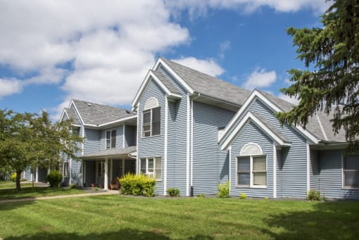 A blue house with a grey roof and a tree in front.