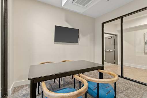 A conference room with a table, chairs, and a television on the wall.