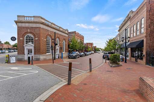 A street view of a town with a brick building on the left and a parking lot in the foreground.