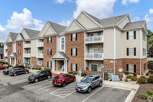 A parking lot in front of a multi-story apartment building with cars parked.
