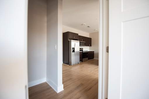 A kitchen with white walls and wooden floors is visible through an open door.