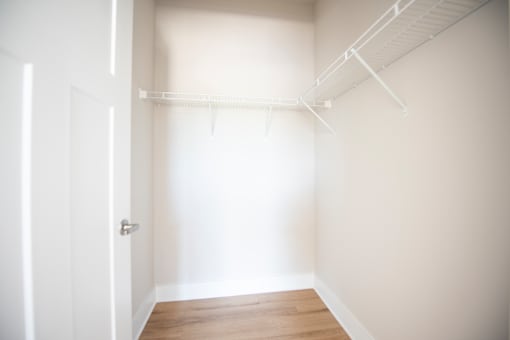 A white door is on the left of a room with a white wall and a white shelf.
