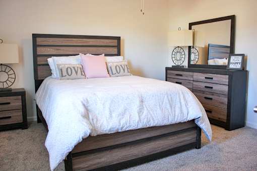 A bed with a white comforter and two pink pillows with the word LOVE on them.
