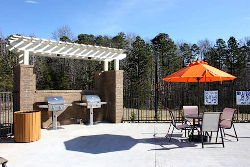 A patio with a grill and chairs under a white pergola.