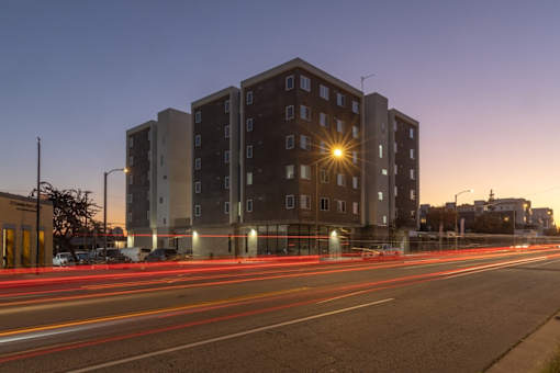 A long exposure shot of a street with a building in the background and light trails from moving vehicles.