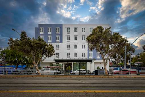 A modern white building with blue trim is surrounded by trees and street lights.