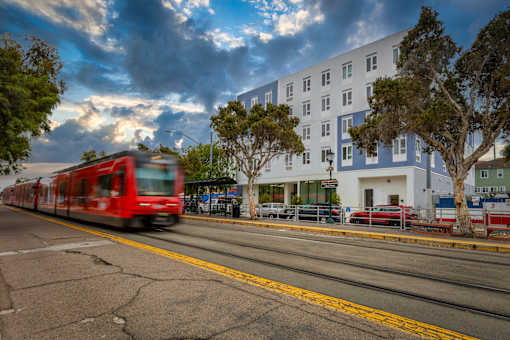 A red train is passing by a white building.