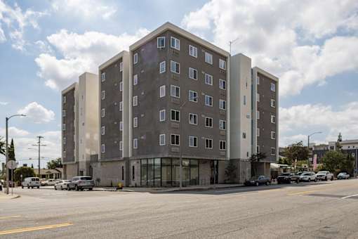 A large grey building with many windows sits on a street corner.