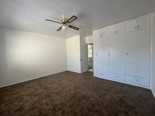 A room with a ceiling fan and brown carpet.