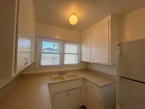 A kitchen with white cabinets and a window with blinds.