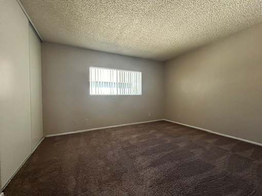 A room with a carpeted floor and a window with blinds.