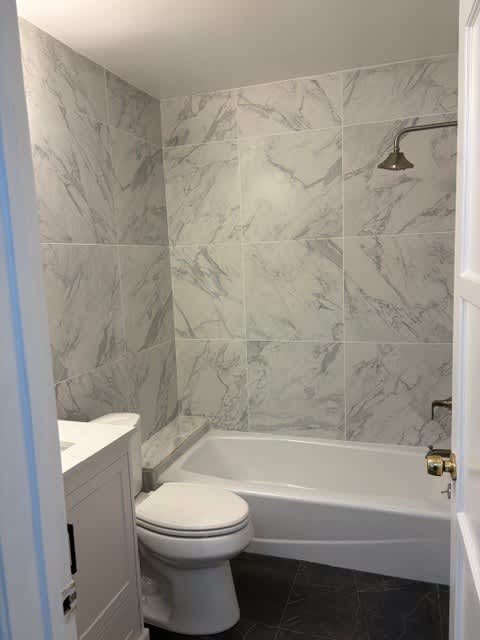 A white toilet sits in a bathroom with marble tile walls.