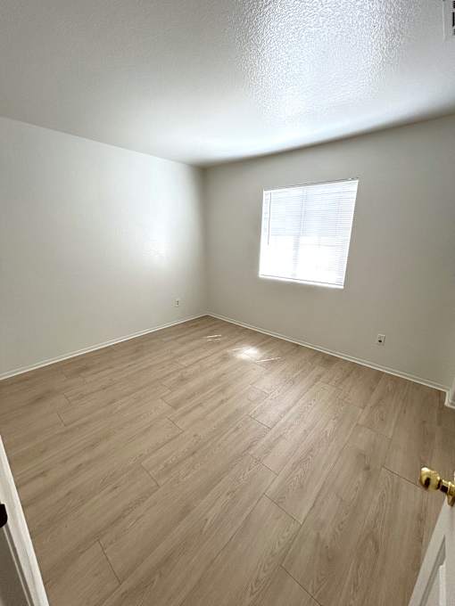 A room with a wooden floor and a window with blinds.