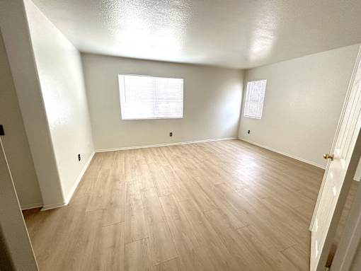 A room with wooden flooring and two windows.