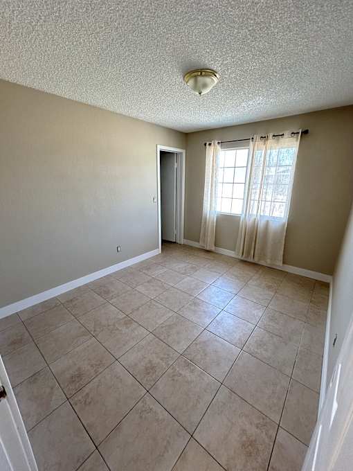 A room with beige walls and tile flooring with a door and window.